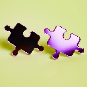 May include: Two purple puzzle piece shaped earrings. The earrings are made of metal and have a shiny finish.