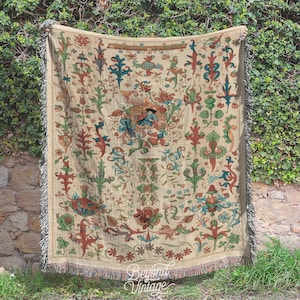 May include: A woven tapestry throw blanket with a cream background and intricate floral patterns in shades of red, green, blue, and gold. The design features stylized leaves, flowers, and vines.