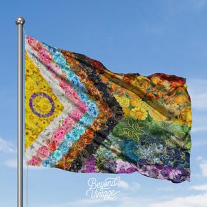 May include: A colorful flag with a floral design, waving in the wind against a blue sky. The flag features a variety of flowers in different colors, including yellow, pink, blue, and orange. The words "Beyond Vintage" are at the bottom.