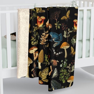 May include: A black fleece throw blanket with a vintage botanical print featuring mushrooms, butterflies, frogs, and plants.