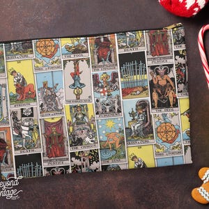 May include: A rectangular zippered pouch featuring a colorful tarot card design. The pouch displays various tarot cards with illustrations and text, including "The Fool," "Death," and "The Devil." The pouch has a black zipper and the words "Beyond Vintage" are printed on the bottom left.