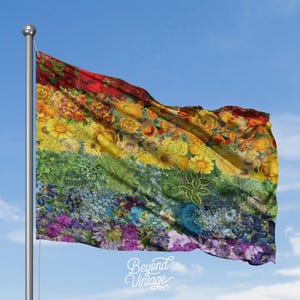 May include: A rainbow flag waving in the wind, composed of various flowers in a spectrum of colors. The flag is mounted on a silver pole against a blue sky. The words "Beyond Vintage" are printed on the bottom.