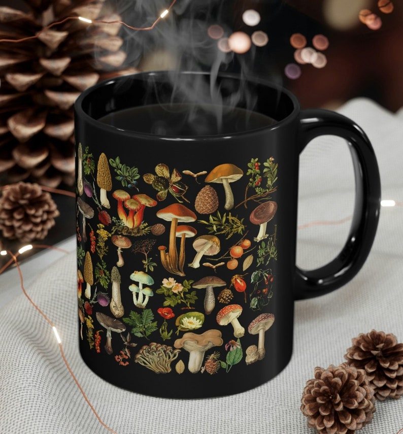 May include: Black ceramic mug with a vintage illustration of various mushrooms and foliage. The mug is filled with coffee and steam is rising from the top.