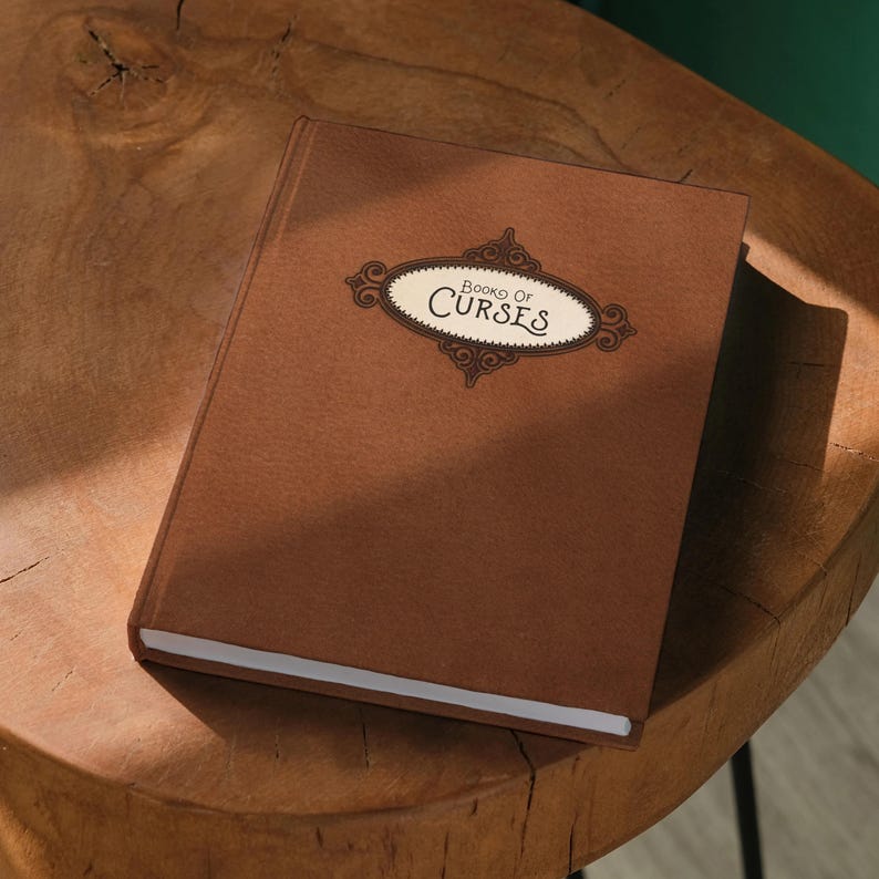 A brown hardcover book titled "Book of Curses" rests on a wooden stool against a green wall.