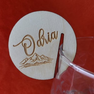 K&ouml;nnte beinhalten: Ein Holz-Getr&auml;nke-Marker mit dem Namen "Olivia" eingraviert. Der Marker hat ein Bergketten-Design und einen Ausschnitt f&uuml;r ein Glas.