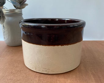 Könnte beinhalten: Ein brauner und weißer glasierter Keramiktopf mit abgerundeter Form. Der Topf hat eine braune Oberseite und eine weiße Unterseite.