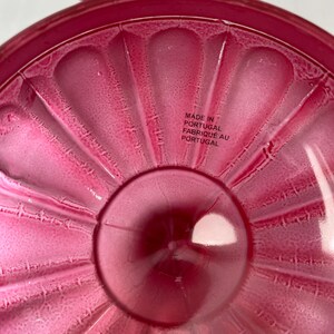 May include: The underside of a pink glass bowl with a scalloped edge. The bowl is made in Portugal, as indicated by the text "Made in Portugal Fabrique au Portugal".