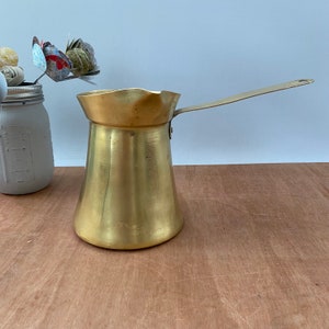 以下が含まれることがあります： 長い取っ手のある金色の金属製のコーヒーポット。ポットは丸みを帯びたボディと注ぎ口を持っています。