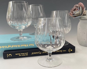 May include: Four clear glass brandy snifters with a diamond pattern on the sides. The glasses are sitting on a stack of books with the titles "The Secret of Great Pyramid" and "Not That Kind of Girl".