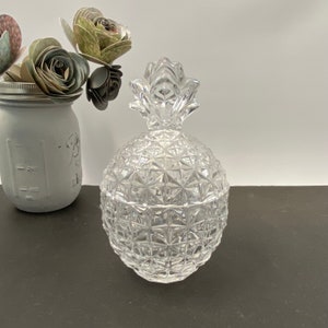 May include: A clear glass pineapple-shaped jar with a textured surface. The jar is empty and has a lid.