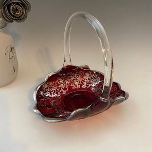 Puede incluir: Un plato de servir de vidrio rojo con un diseño floral plateado y un asa de vidrio transparente. El plato tiene forma de cesta.