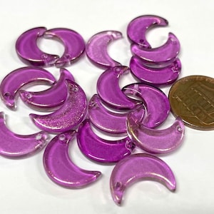 May include: A group of 17 purple glass crescent moon charms with gold glitter accents. The charms have a hole at the top for stringing.