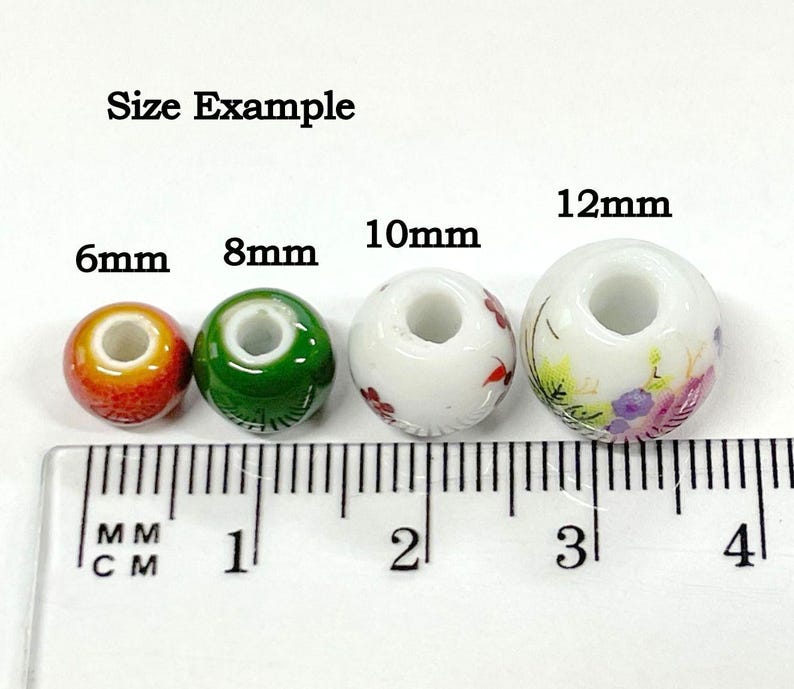 K&ouml;nnte beinhalten: Gr&ouml;&szlig;enbeispiel f&uuml;r vier Keramikperlen mit Blumendesigns. Die Perlen haben einen Durchmesser von 6 mm, 8 mm, 10 mm und 12 mm.