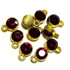 May include: A group of eight gold-toned metal charms with red glass stones. Each charm has a loop for attaching to a necklace, bracelet, or other jewelry.