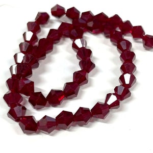 May include: A strand of dark red faceted glass beads. The beads are small and have a pointed shape.