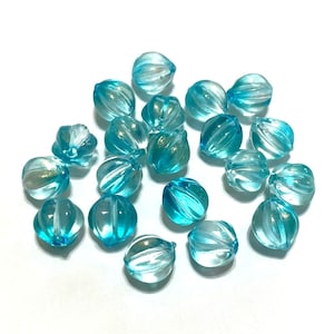 May include: A collection of 18 turquoise blue glass beads with a faceted, starburst design. The beads have a translucent, iridescent finish.