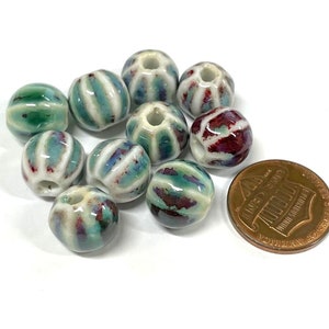 May include: A collection of ten ceramic beads with a white base and green and red stripes. The beads are approximately the size of a UK penny.