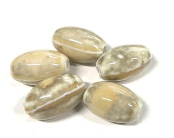 May include: Five oval beads with a glossy finish. The beads are mainly beige with streaks of white and brown. Each bead has a hole through the centre, suggesting they are for stringing. The beads are arranged in a circular pattern.