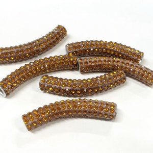 May include: A group of six brown, curved, rhinestone-covered beads. The beads are all the same size and shape, and they are arranged in a loose pile.