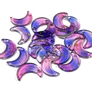 May include: A collection of crescent moon shaped glass beads with a gradient of pink and purple colors and gold flecks.