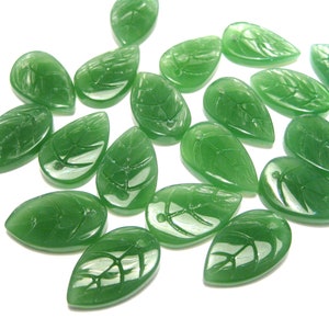 May include: A collection of green glass leaf-shaped beads with a carved design. The beads are translucent and have a glossy finish.