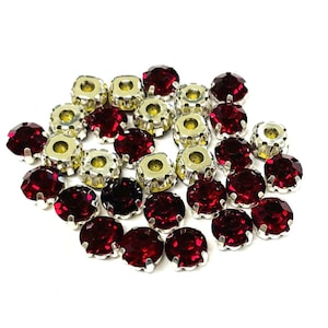 May include: A group of red rhinestone embellishments with silver settings. The rhinestones are round and have a faceted finish.