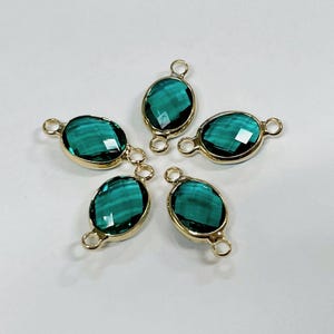 May include: Five oval-shaped teal-colored gemstone connectors with gold-colored metal settings. Each gem has a faceted surface and is connected to a small loop on each end. The connectors are arranged in a starburst pattern.