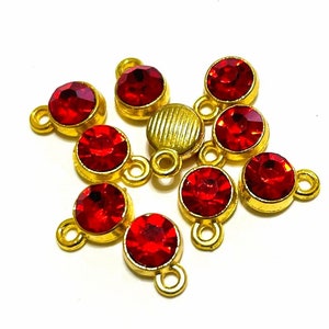 May include: A group of eight red rhinestone charms with gold-toned metal loops. The charms are arranged in a cluster on a white background.