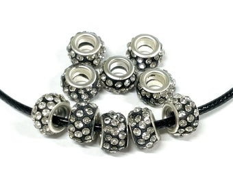 May include: A set of ten silver-toned spacer beads with clear rhinestones. The beads are round and have a hole in the center. They are strung on a black cord.