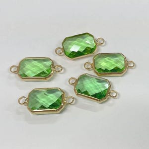 May include: Five green rectangular gemstone connectors with gold-coloured frames and small loops on each end. The gemstones have a faceted cut, reflecting light. Suitable for jewellery making.