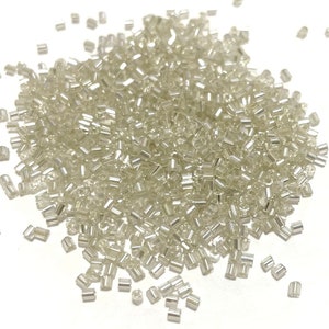 May include: A large pile of small, clear glass beads with a silver iridescent finish. The beads are scattered on a white background.