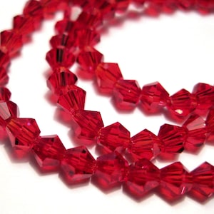 May include: Close-up of strands of faceted, bright red beads. The beads are strung together, creating a flowing, curved pattern. The beads have a glossy, reflective surface, catching the light and creating a sparkling effect. The beads are likely for jewelry making.