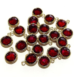 May include: A group of 18 red glass beads with gold-toned metal accents. Each bead has a small loop on the top for attaching to jewelry or other crafts.
