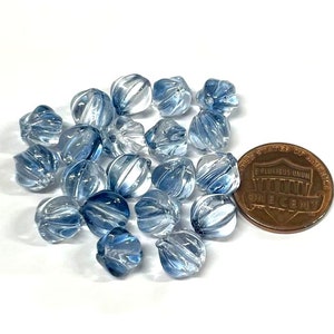 May include: A group of light blue glass beads with a swirl design. The beads are approximately the size of a US penny.