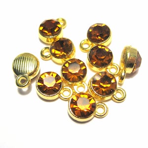 May include: A group of eight gold-toned metal charms with amber-colored glass stones. Each charm has a loop for attaching to a necklace, bracelet, or other jewelry.