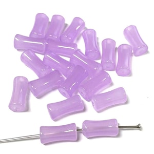 May include: A collection of 20 lavender glass beads, each with a slightly curved shape. The beads are arranged in a loose pile on a white surface.