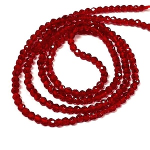 May include: Strands of faceted, deep red beads. The beads are small and uniform in size, strung together to form multiple strands. The beads have a sparkling, reflective quality, suggesting they are made of glass or crystal. The background is plain white.