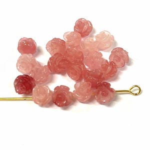 May include: A collection of pink rose-shaped beads made of rose quartz. The beads are arranged in a gradient from light pink to dark pink.
