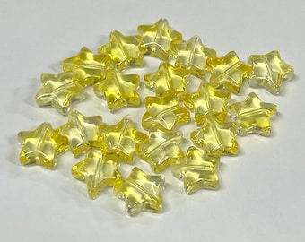 May include: A collection of small, translucent yellow star-shaped beads. Each bead features a five-pointed star design with a visible hole running through the center for stringing. The beads have a smooth, glossy finish and a clear, light yellow color.