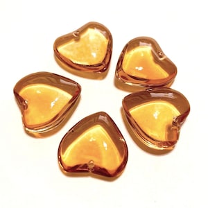 May include: Five amber glass heart-shaped charms. The charms are translucent and have a slight shimmer.