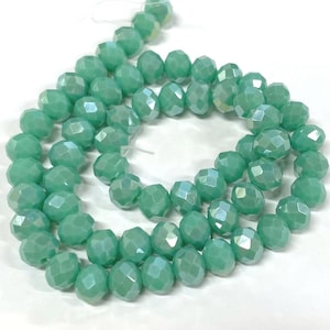 May include: A strand of light green faceted glass beads. The beads are round and have a slightly iridescent finish.