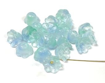 May include: A collection of light blue and green glass flower beads. The beads are translucent and have a delicate, floral design.