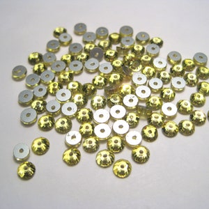 May include: A large pile of yellow, round, flat-backed rhinestones with a silver backing.