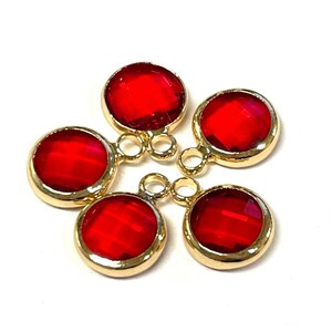 May include: Five red glass round charms with gold metal frames and jump rings. The charms are approximately 1 inch in diameter.