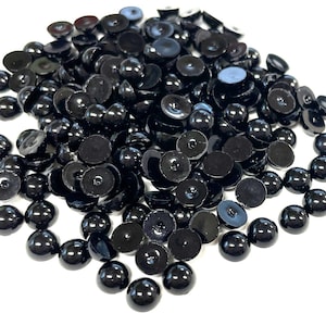 May include: A large pile of black plastic doll eyes. The eyes are round and have a flat back.