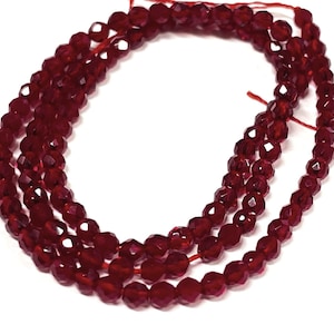 May include: A strand of deep red faceted glass beads. The beads are strung on a thin red thread.