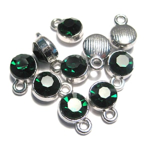May include: A group of ten silver-toned charms with emerald green rhinestones. Each charm has a loop for attaching to a bracelet or necklace.