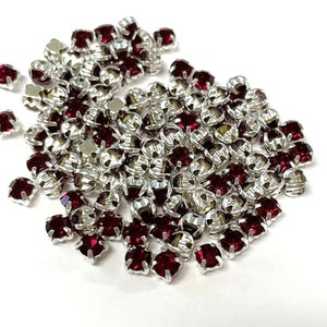 May include: A large pile of red rhinestone embellishments with silver settings. The rhinestones are all the same size and shape, and they are arranged in a random pattern.