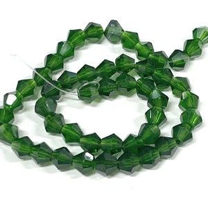 May include: A strand of dark green faceted glass beads. The beads are strung on a clear thread and are arranged in a circular pattern.