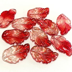 May include: A group of ten red and clear glass leaf-shaped beads. The beads are translucent and have a shimmery finish.